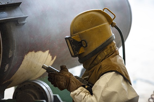 Worker in safety gear sandblasting metal surface